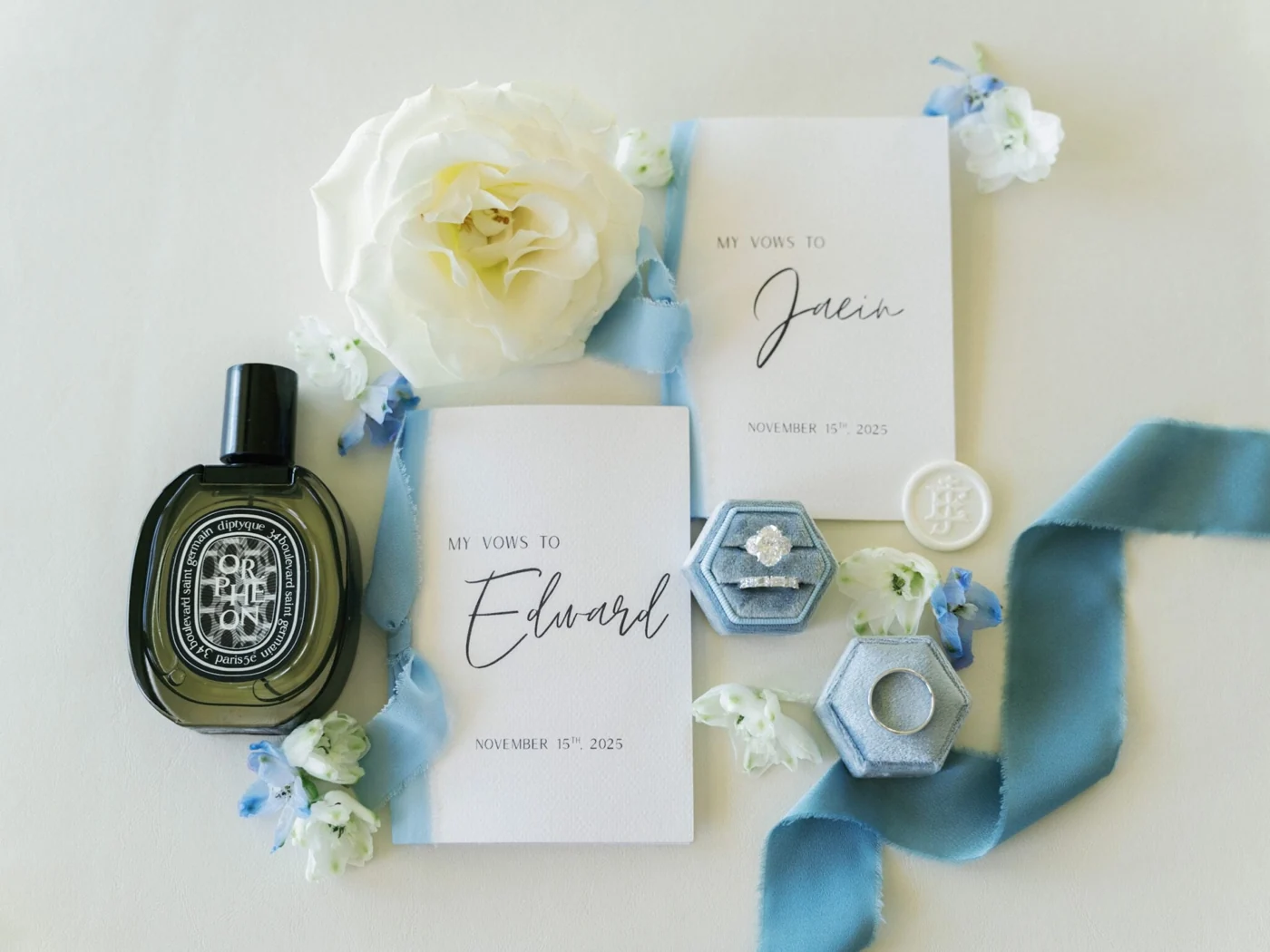 Wedding invitations, rings and perfume arranged with pale blue ribbons