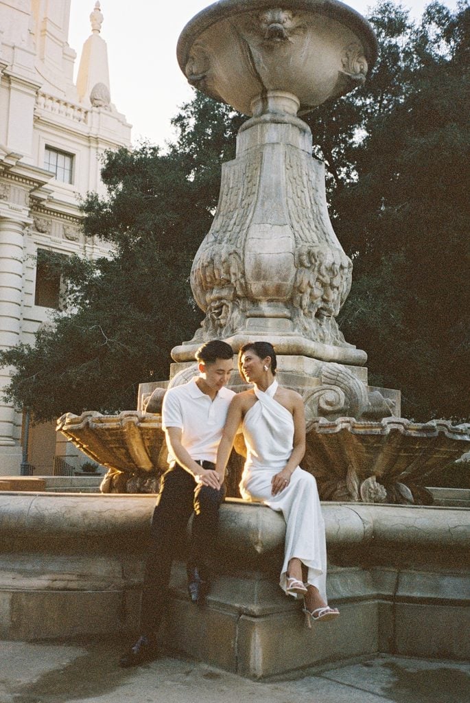 Newlyweds sitting on historical city fountain edge for luxury blue hour wedding photos