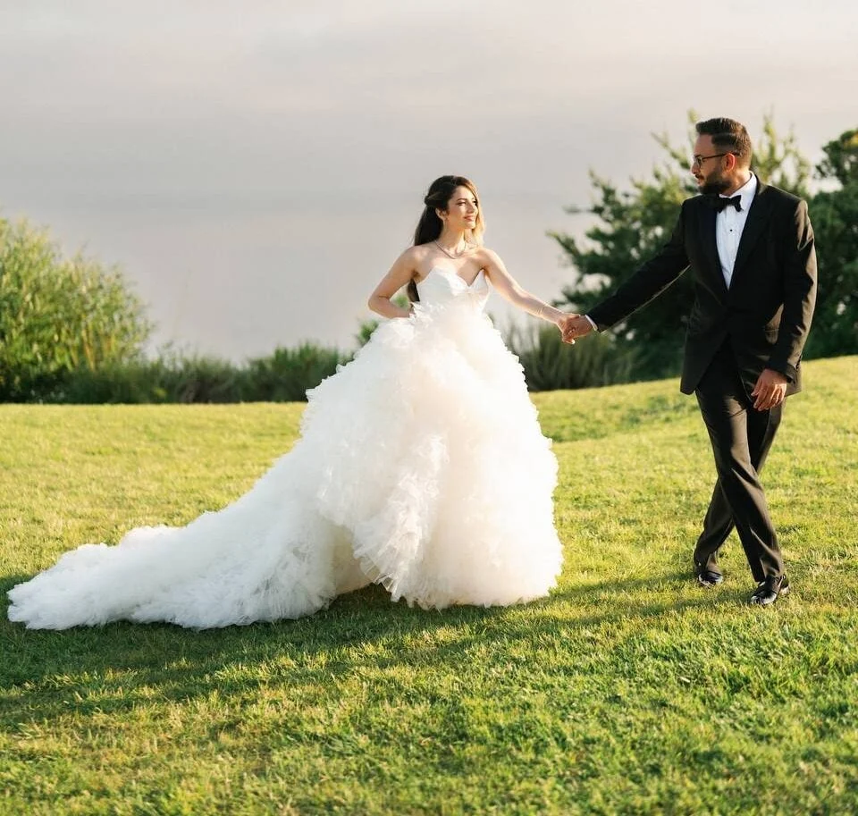 Bride and groom holding hands on a lawn, with the bride’s train behind her