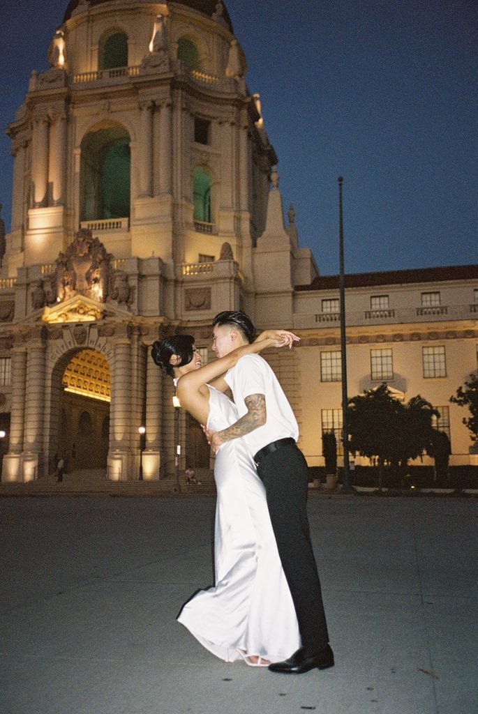 Modern newlyweds posing near beautiful city tower architecture for blue hour wedding photos