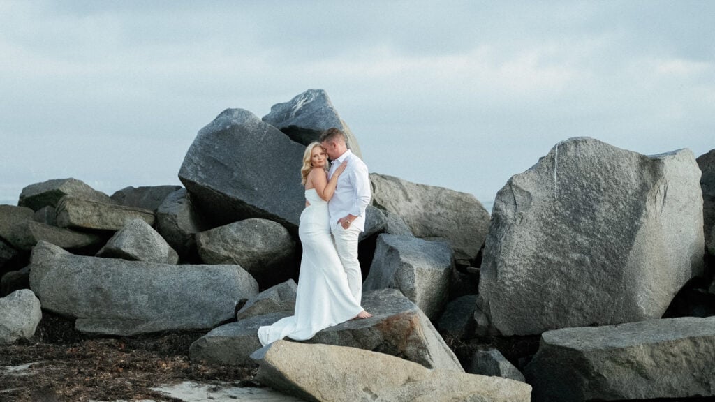 Wide shot of wedding couple embracing on ocean rocks luxury blue hour wedding photos