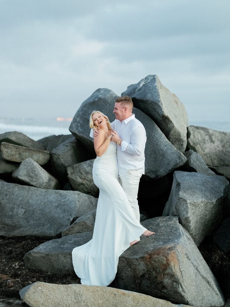 Newlyweds laughing on big coastal rocks luxury blue hour wedding photos